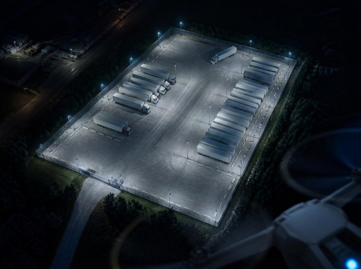Aerial night view of a small fenced truck yard with lit trailer rows, seen from a drone